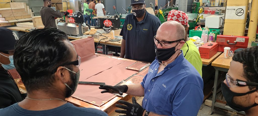 Picture of a soldering class with students and a teacher having a conversation.