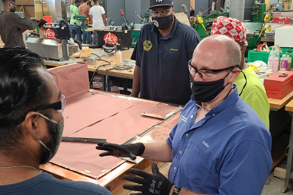 Picture of a soldering class with students and a teacher having a conversation.