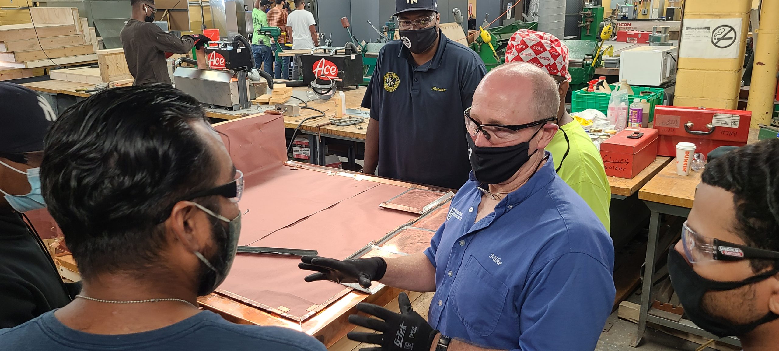 Picture of a soldering class with students and a teacher having a conversation.