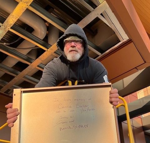 Man holding a white board with "in loving memory" written for Carrie Barber.