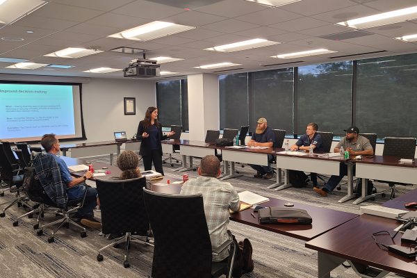 People sitting at tables listening to a speaker at the front of the room.