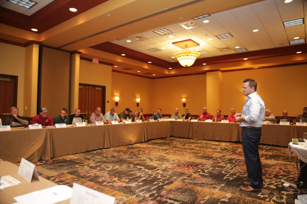An instructor presenting to a room of people at tables.